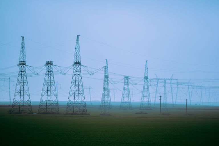 Industrial station with rows of transmission towers with curved wires on green meadow under blue sky